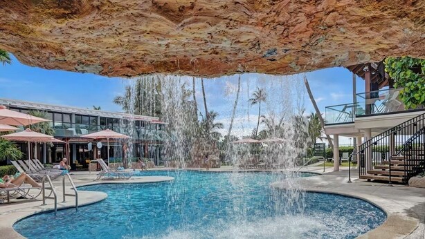 Une piscine agrémentée d’une cascade, de chaises longues et de parasols.
