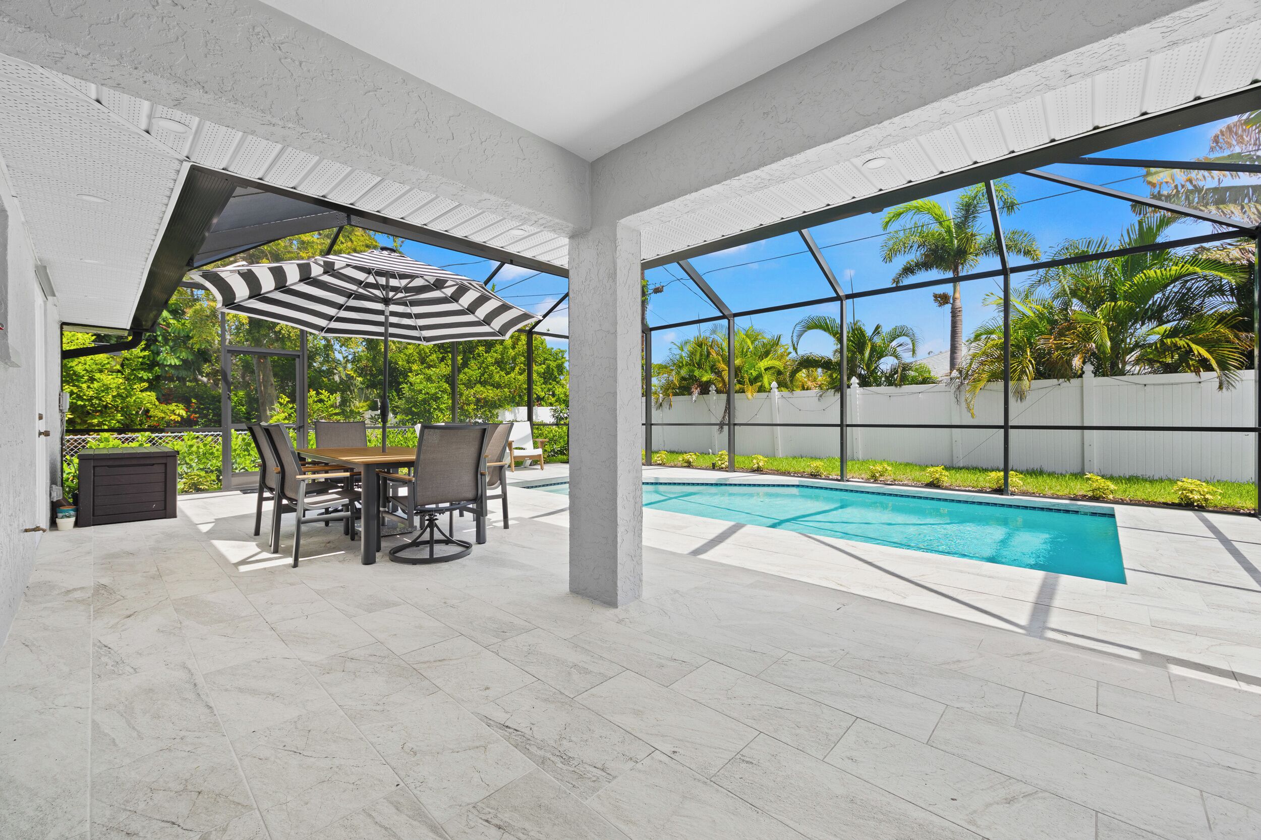 Une terrasse couverte avec une piscine, du mobilier d’extérieur et une vue sur les palmiers.