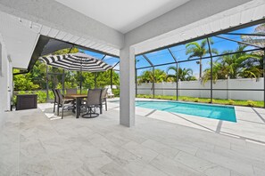 Une terrasse couverte avec une piscine, du mobilier d’extérieur et une vue sur les palmiers.