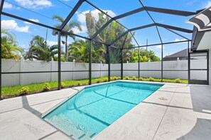A swimming pool with a clear blue water, surrounded by a white fence, and a metal structure overhead. - The Coastal Haven | Heated Pool | Near Beach (Naples)