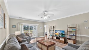 A living room with a sofa, coffee table, TV, and a ceiling fan. - Relax at Magnolia Pointe — Minutes from the Beah | Magnolia Pointe Luster Leaf 4882-202 (Myrtle Beach)