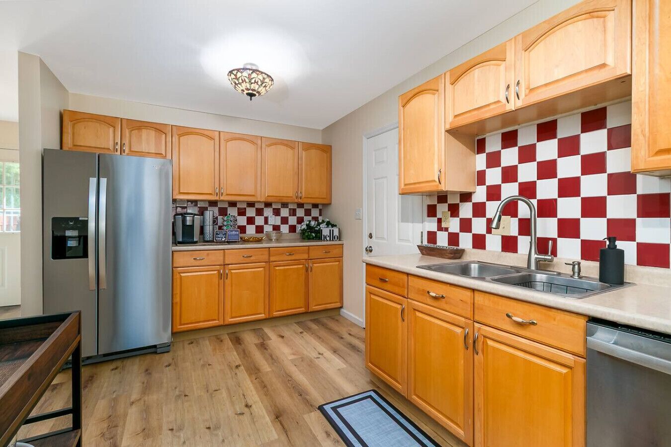 A kitchen with wooden cabinets, a stainless steel refrigerator, a checkered backsplash, and a sink.