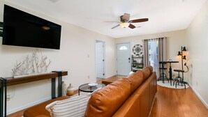 A living room with a brown leather sofa, a flat-screen TV, a ceiling fan, and a dining area with stools. - Charming Historic Retreat in Old Town St. Charles (Saint Charles)