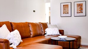 A modern living room with a brown leather sofa, a round coffee table, and two framed artworks on the wall. - Charming Historic Retreat in Old Town St. Charles (Saint Charles)