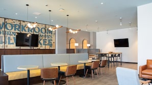 A modern workspace with a large wall-mounted TV, multiple tables, and seating areas.