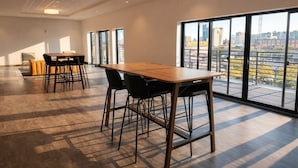 A spacious room with a large table and chairs, large windows with a city view, and a high ceiling with recessed lighting.