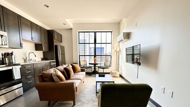 A modern kitchen with dark cabinets, a stainless steel refrigerator, and a dining area with a table and chairs.