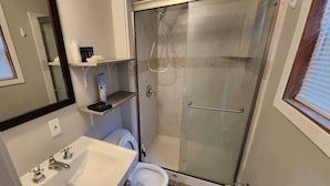 Un baño con ducha de vidrio, lavamanos blanco y retrete.