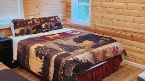 Un dormitorio tipo cabaña de troncos con cama, mesita de noche, ventana y suelo de madera.