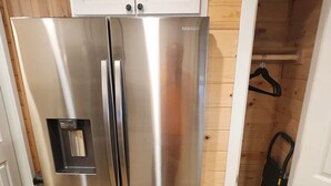 Un refrigerador de acero inoxidable en una cocina con paredes de madera y una puerta blanca.