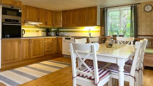 A kitchen with wooden cabinets, a dining table with white chairs, and a window with curtains. - 2 bedroom awesome home in Arboga (Arboga)