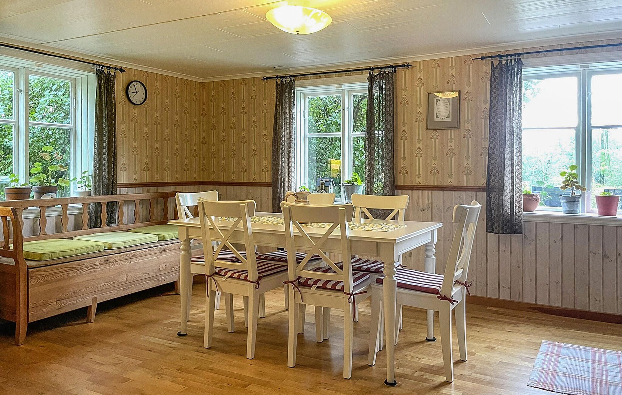 A cozy dining area with a wooden table and chairs, a bench with cushions, and large windows with curtains.
