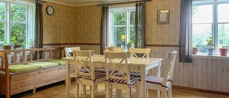 A cozy dining area with a wooden table and chairs, a bench with cushions, and large windows with curtains.