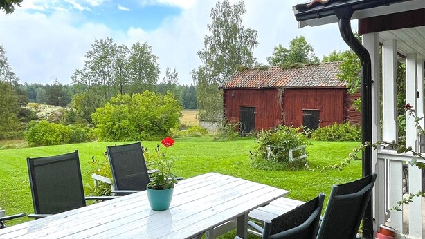 A wooden table with chairs, a potted plant, and a view of a red barn in a green landscape. - 2 bedroom awesome home in Arboga (Arboga)