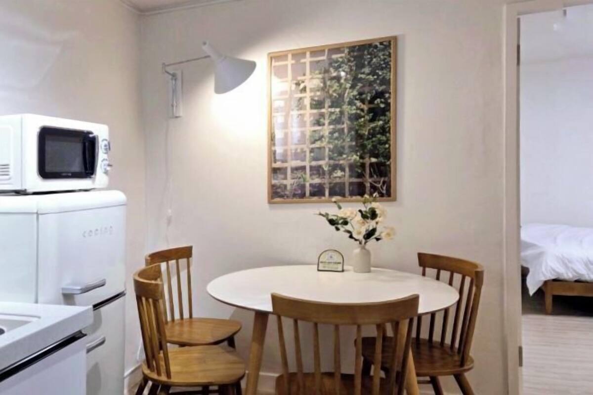 A compact kitchen with a microwave, a dining table with four chairs, and a decorative plant on the wall.