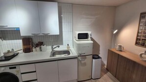 A compact kitchen with white cabinets, a microwave, a sink, and a small trash bin. - Stay Aurora (Seoul)
