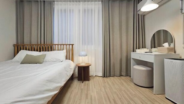 A hotel room with a bed, bedside table, lamp, vanity with mirror, and a large speaker. - Stay Aurora (Seoul)