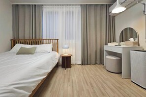 Une chambre d’hôtel comprenant un lit, une table de chevet, une lampe, une coiffeuse avec miroir et une grande enceinte.