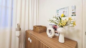 A hotel room with a wooden cabinet, a wicker basket, a white vase with flowers, and a magazine on the wall. - Stay Aurora (Seoul)