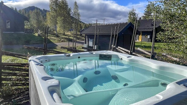 Un bain à remous installé dans un cadre naturel, avec une terrasse en bois et une vue sur une montagne.