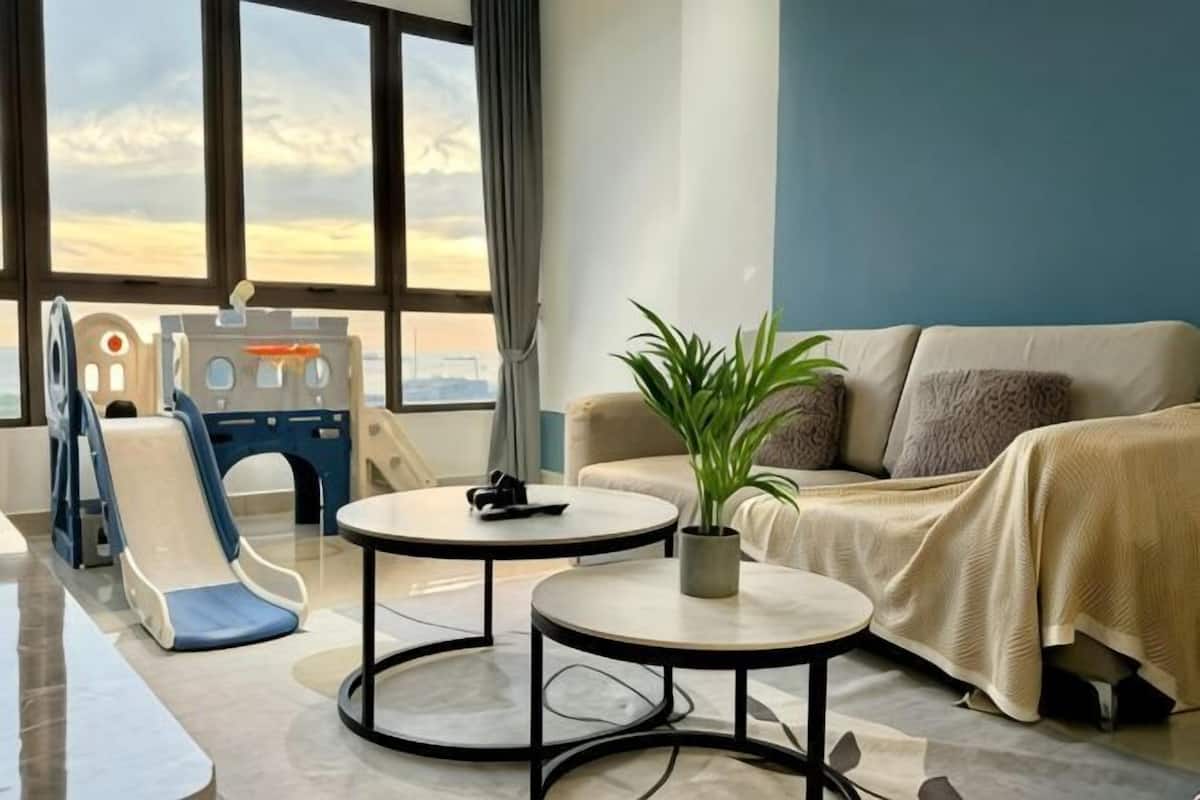 A living room with a sofa, two coffee tables, a plant, and a play area with a slide.