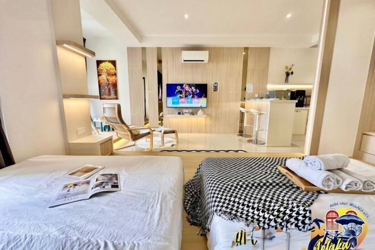 A hotel room with two beds, a TV, a desk, and a kitchenette.