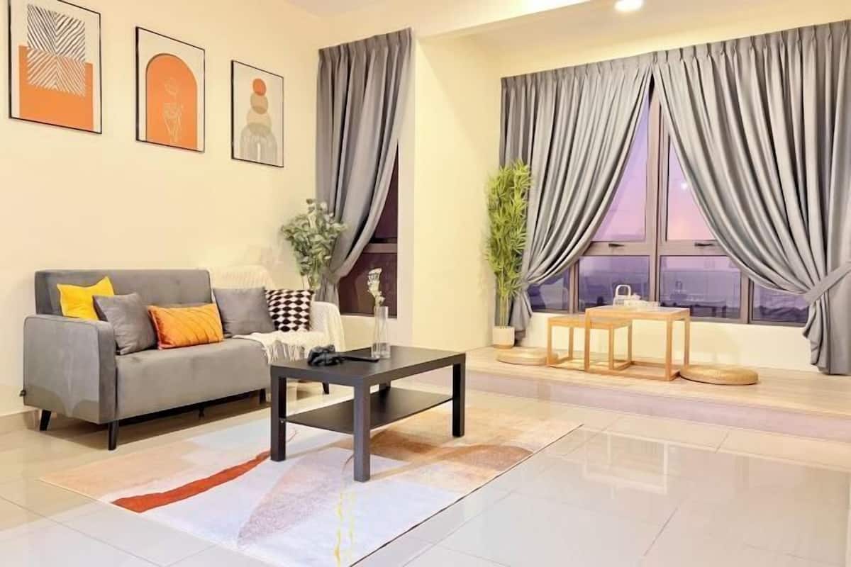 A modern living room with a sofa, coffee table, and a view through large windows with curtains.