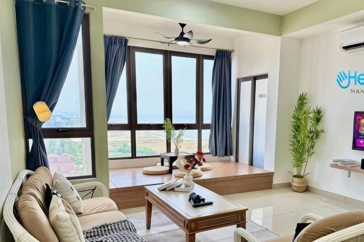 A modern living room with a sofa, a coffee table, and a view of the outdoors through large windows.