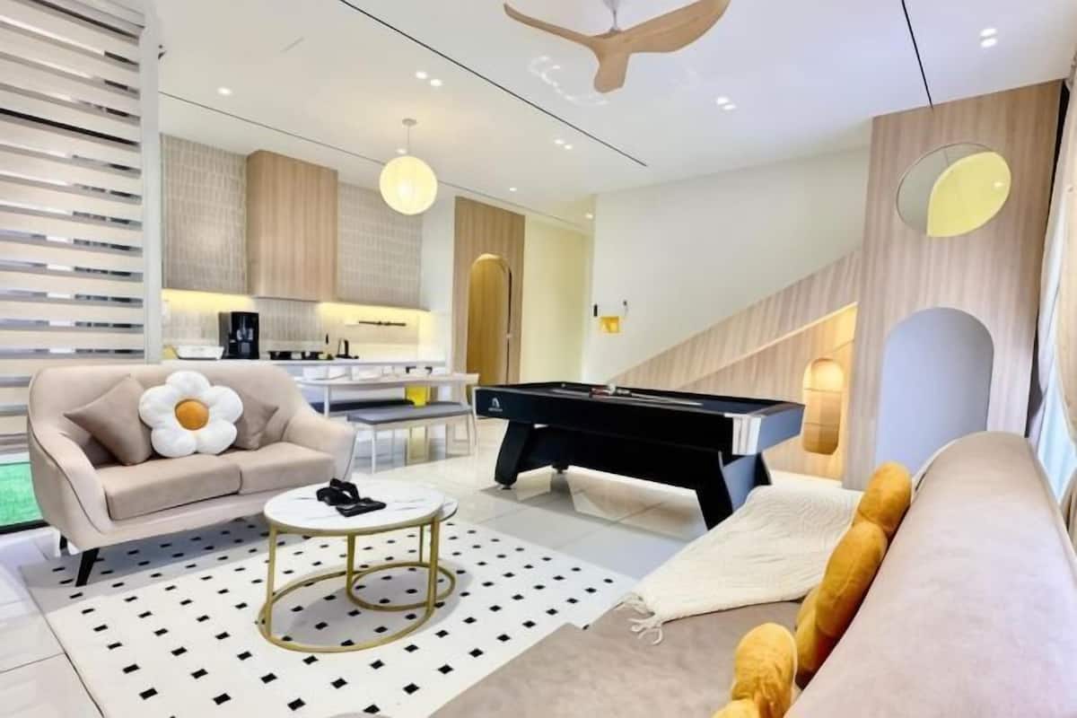 A modern living room with a pool table, sofa, and a kitchen area in the background.