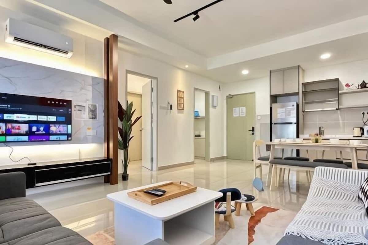 A modern living room with a flat-screen TV, a coffee table, a sofa, and a dining area with a table and chairs.