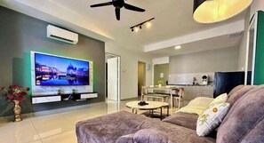 A modern living room with a flat-screen TV, a ceiling fan, a dining area, and a kitchen in the background. - Bali Residence Melaka by Heystay Management (Melaka)