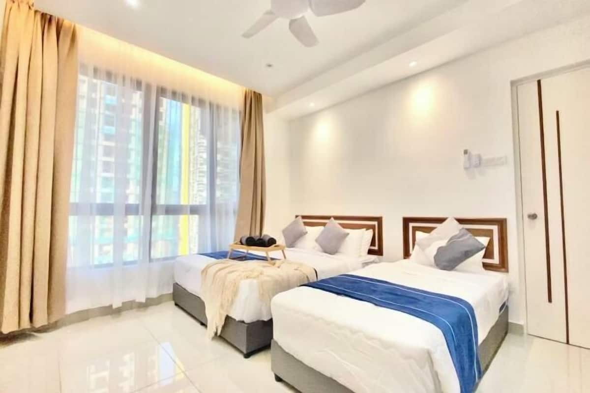 A hotel room with two beds, a ceiling fan, a window with curtains, and a door.