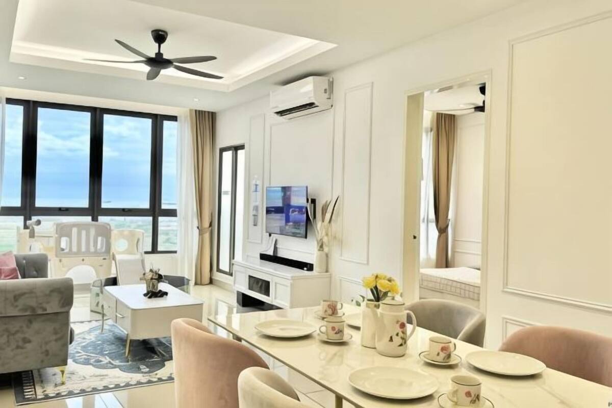 A modern hotel room with a dining area, a sofa, a TV, and a view of the sea.