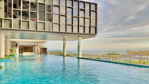 A modern hotel with a rooftop pool overlooking a beach.