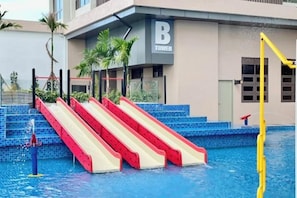 A swimming pool with a red and white slide, a yellow diving board, and a building with a 'B' sign. - Bali Residence Melaka by Heystay Management (Melaka)