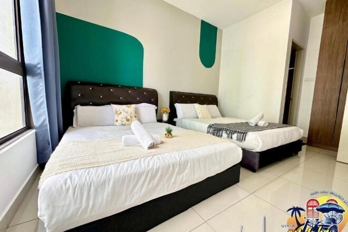 A hotel room with two beds, a teal accent wall, and a window with curtains.