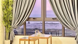 A room with a view of a snowy landscape through large windows, a small wooden table with a teapot and glasses, and a bamboo plant beside the windows.