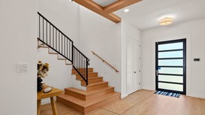 Un intérieur moderne avec un escalier en bois, une porte dotée d’un panneau de verre et une petite table sur laquelle est posé un vase.