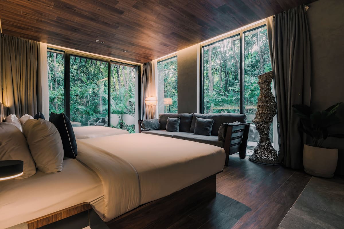 Een moderne slaapkamer met een groot bed, een sofa en uitzicht op weelderige begroeiing door grote ramen.