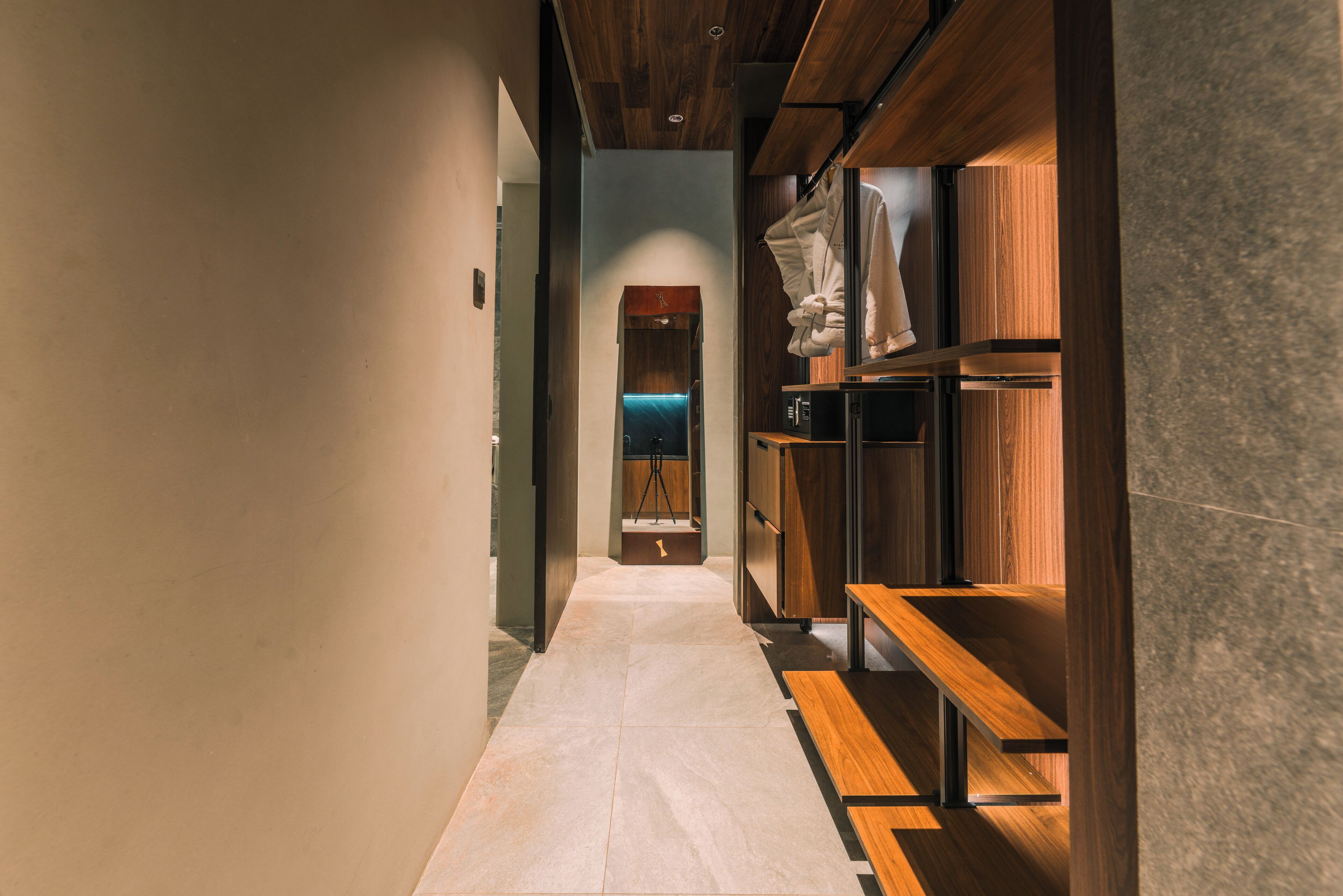 A hallway with a wooden bench, a robe rack, and a tripod in the background.
