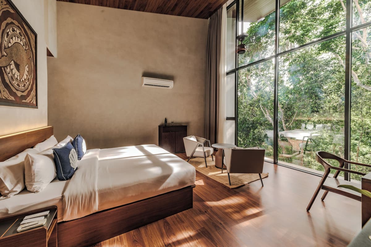 Een moderne slaapkamer met een groot bed, een klein bureau en uitzicht op het groen.