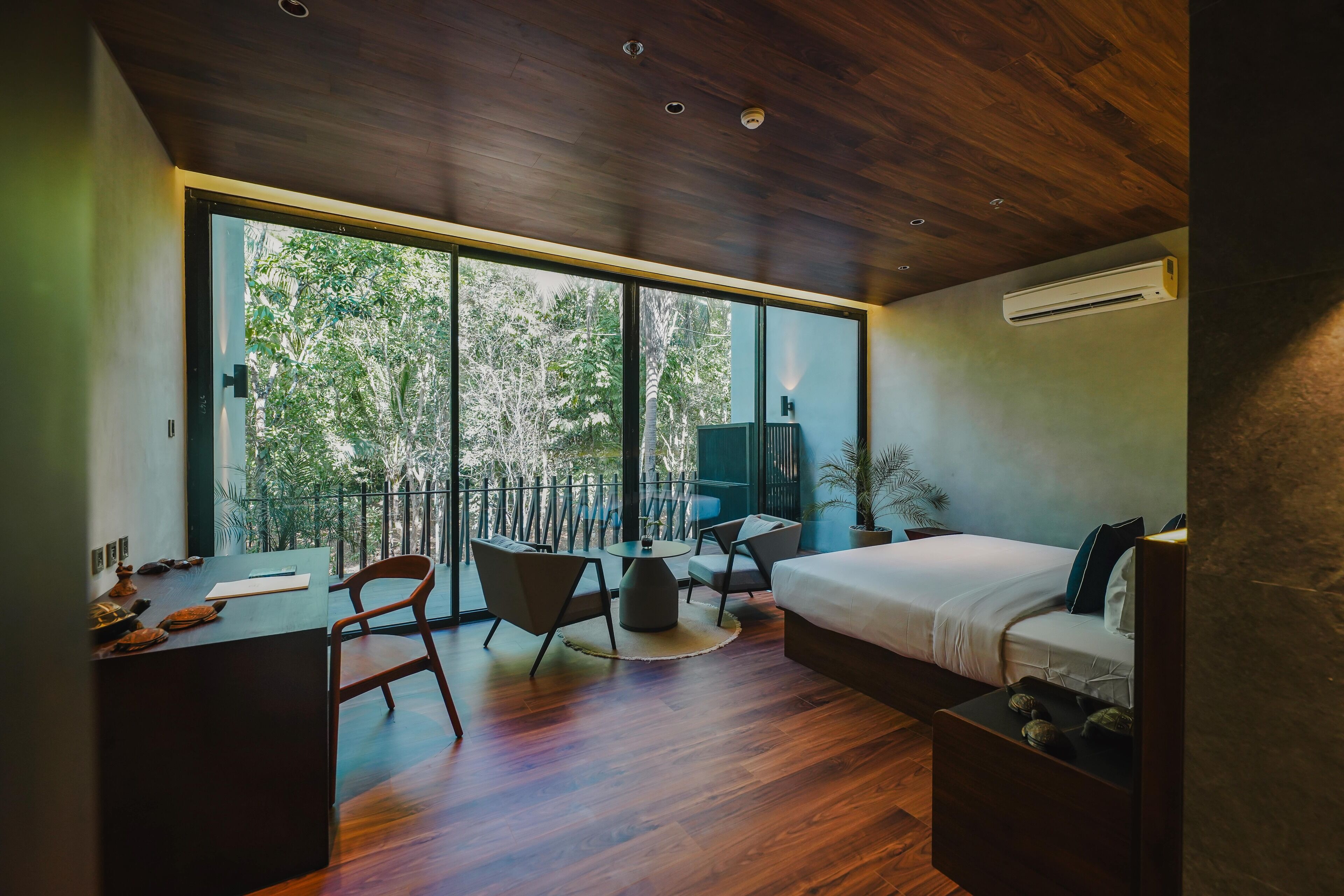 A modern bedroom with a large window, a desk, a bed, and a small table.