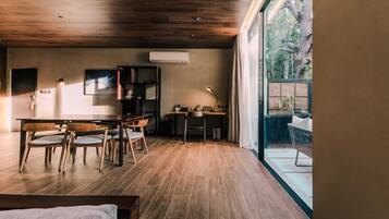 Una habitación moderna con techo de madera, una mesa de comedor con sillas, un escritorio con silla, una lámpara de pie y vistas a zonas verdes al exterior.