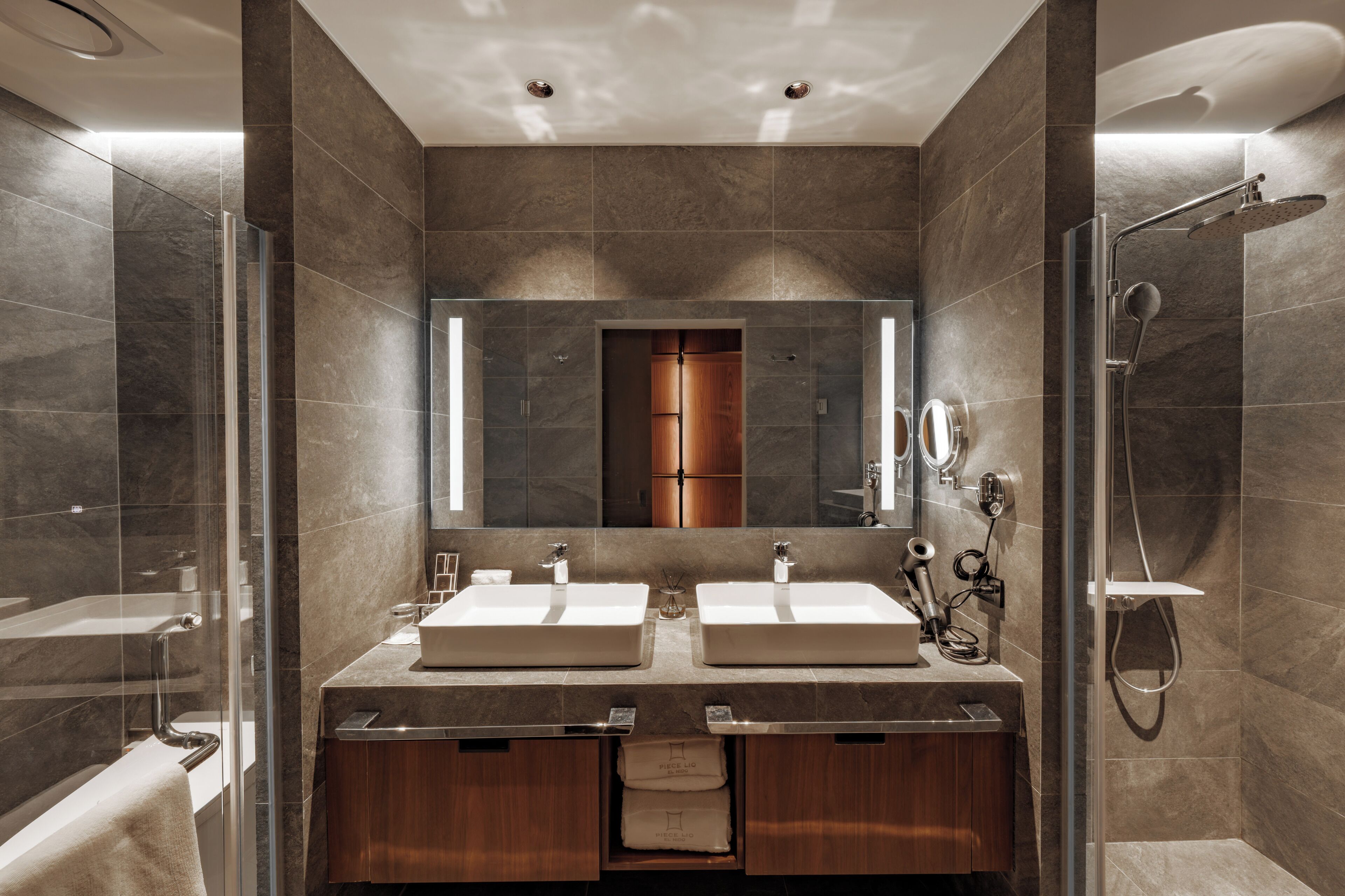 A modern bathroom with two sinks, a shower, and a mirror.