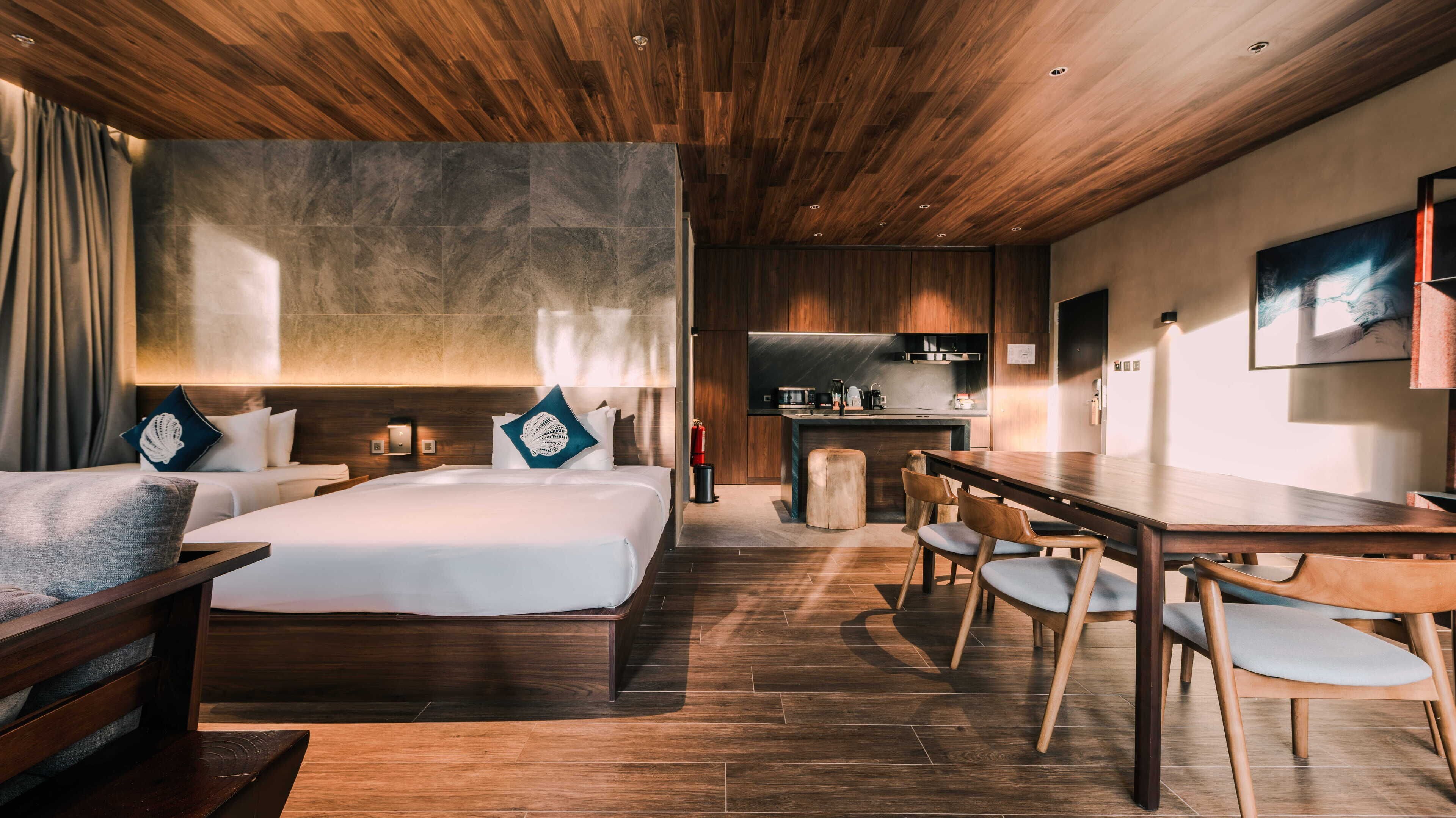Een moderne hotelkamer met een groot bed, een houten eettafel en een kitchenette.