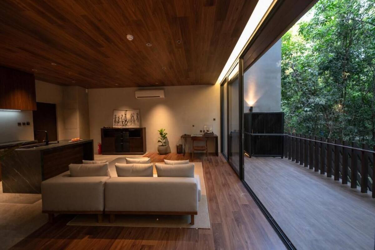 Een modern interieur met een houten plafond, een bank, een keukenhoek en een balkon met uitzicht op bomen.