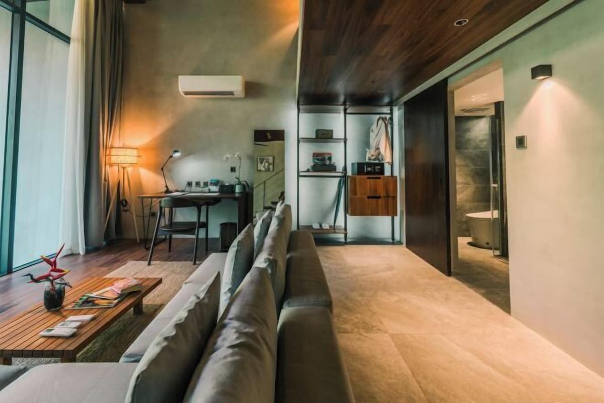 Una sala de estar moderna con sofá, mesa de comedor y zona de cocina con refrigerador y estanterías.