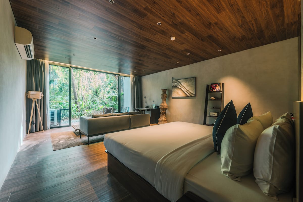 Een slaapkamer met een groot bed, een bank, een bureau en uitzicht op groen buiten het raam.
