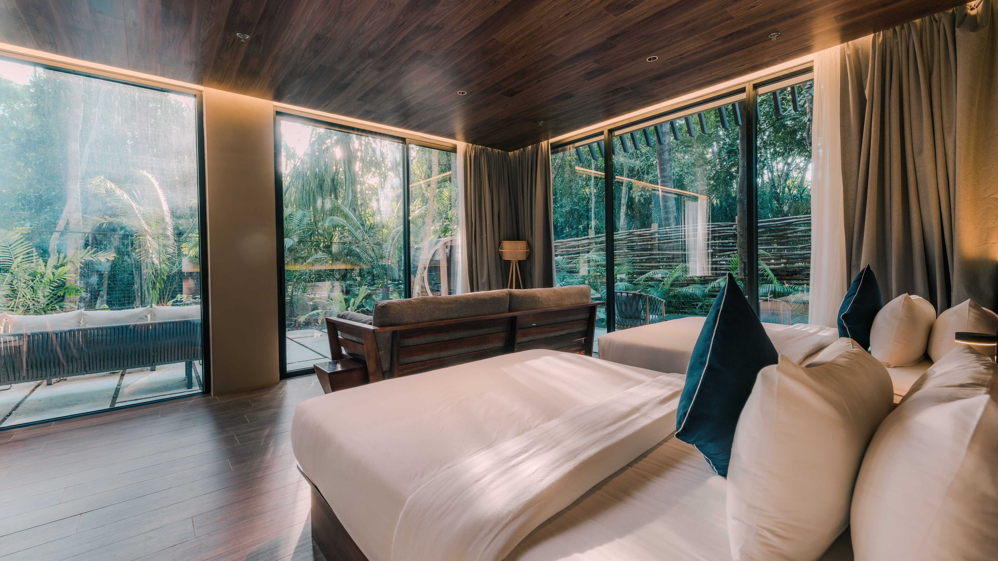 A bedroom with a large bed, a desk, and a view of a tropical garden.