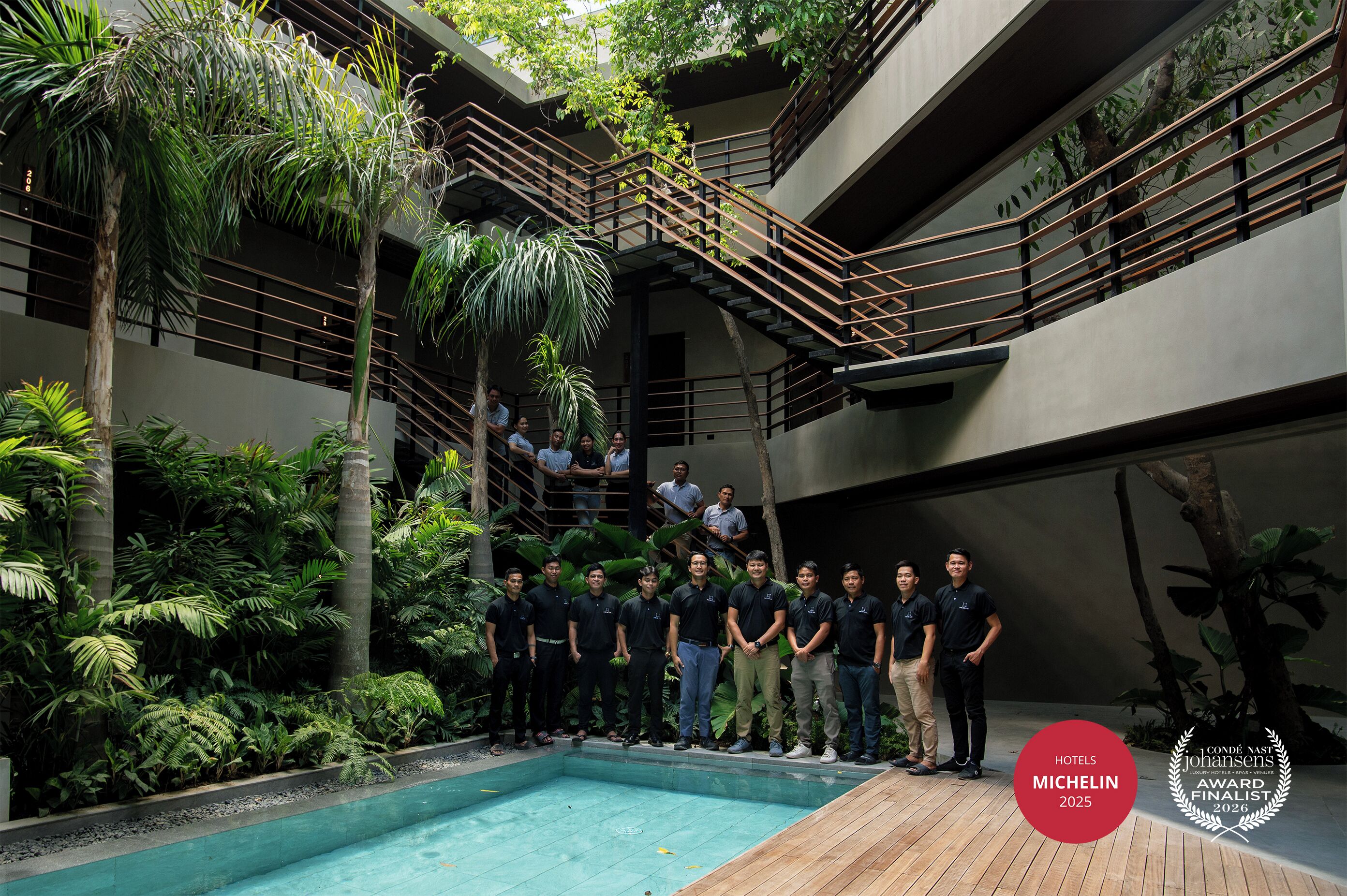 A group of people standing by a pool in a modern building with multiple levels and outdoor greenery.